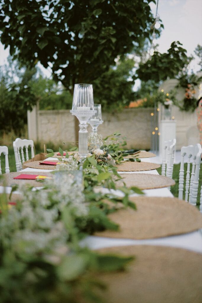 Beautifully decorated outdoor table with green foliage and glass candle holders, perfect for weddings.