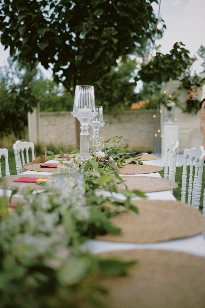 Beautifully decorated outdoor table with green foliage and glass candle holders, perfect for weddings.